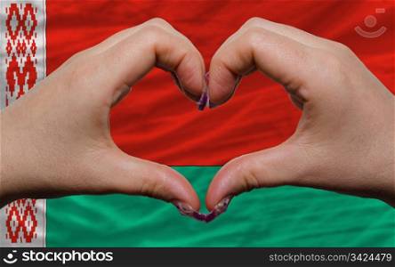 Gesture made by hands showing symbol of heart and love over national belarus flag
