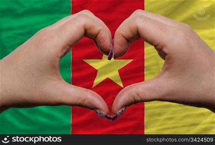 Gesture made by hands showing symbol of heart and love over national cameroon flag