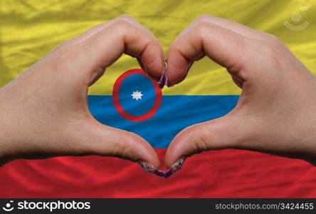 Gesture made by hands showing symbol of heart and love over national colombia flag