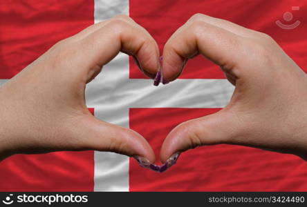 Gesture made by hands showing symbol of heart and love over national denmark flag