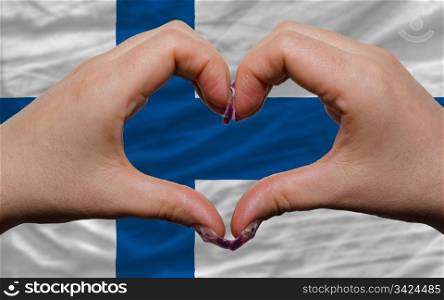 Gesture made by hands showing symbol of heart and love over national finland flag