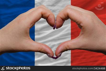 Gesture made by hands showing symbol of heart and love over national france flag