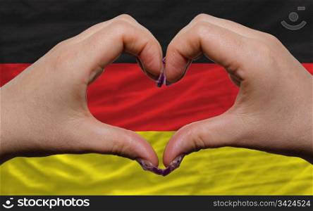 Gesture made by hands showing symbol of heart and love over national germany flag