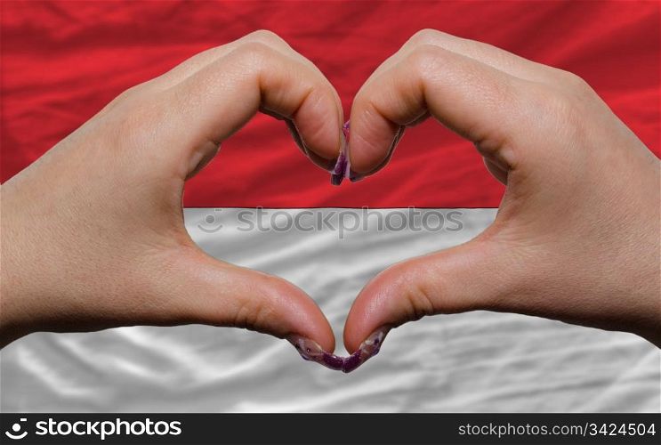 Gesture made by hands showing symbol of heart and love over national indonesia flag