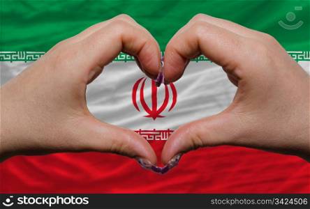 Gesture made by hands showing symbol of heart and love over national iran flag