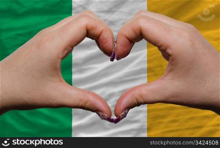 Gesture made by hands showing symbol of heart and love over national ireland flag