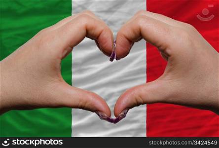 Gesture made by hands showing symbol of heart and love over national italy flag