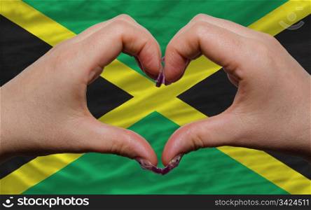 Gesture made by hands showing symbol of heart and love over national jamaica flag