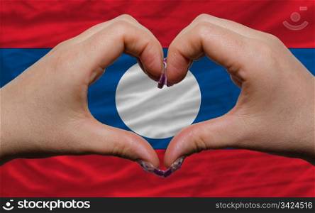 Gesture made by hands showing symbol of heart and love over national laos flag