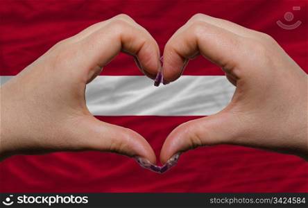 Gesture made by hands showing symbol of heart and love over national latvia flag