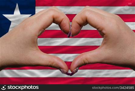 Gesture made by hands showing symbol of heart and love over national liberia flag