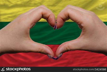 Gesture made by hands showing symbol of heart and love over national lithuania flag