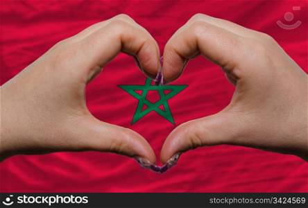 Gesture made by hands showing symbol of heart and love over national morocco flag