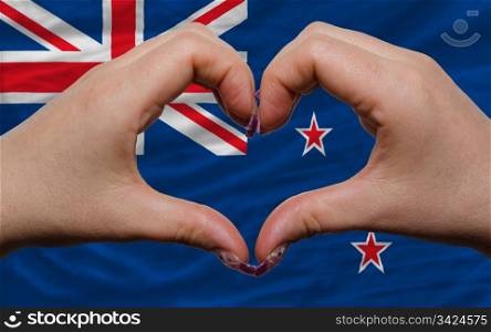 Gesture made by hands showing symbol of heart and love over national new zealand flag