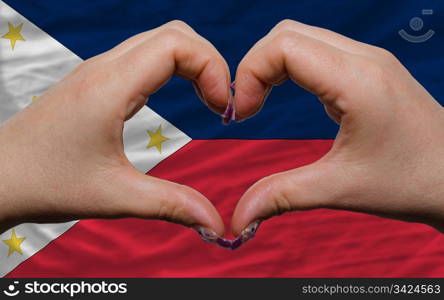 Gesture made by hands showing symbol of heart and love over national philippines flag