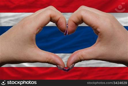 Gesture made by hands showing symbol of heart and love over national thailand flag