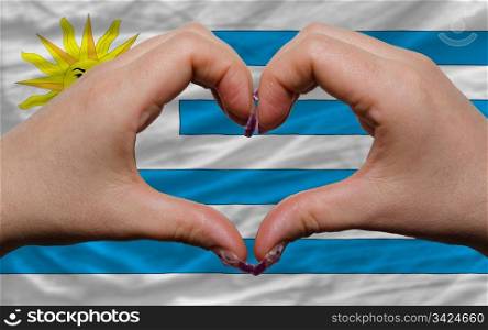 Gesture made by hands showing symbol of heart and love over national uruguay flag