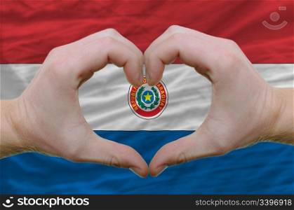 Gesture made by hands showing symbol of heart and love over paraguay flag