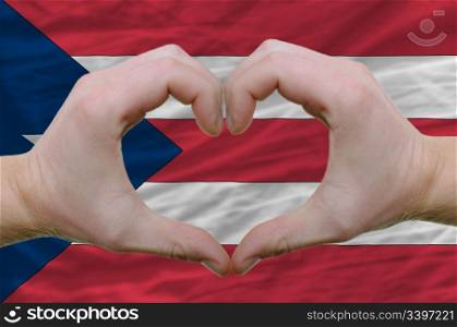 Gesture made by hands showing symbol of heart and love over puertorico flag