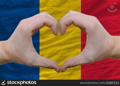 Gesture made by hands showing symbol of heart and love over romania flag