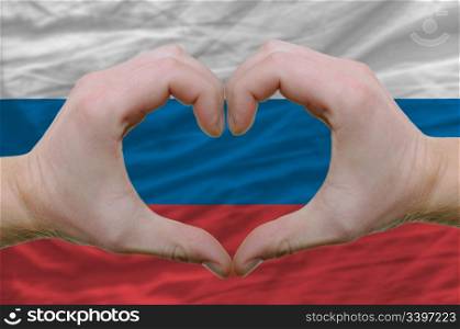 Gesture made by hands showing symbol of heart and love over russia flag