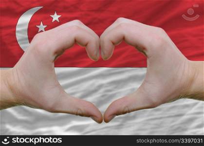 Gesture made by hands showing symbol of heart and love over singapore flag