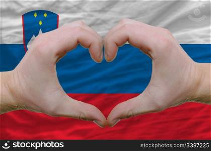 Gesture made by hands showing symbol of heart and love over slovenia flag