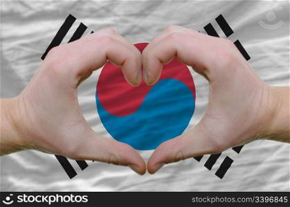 Gesture made by hands showing symbol of heart and love over south korean flag
