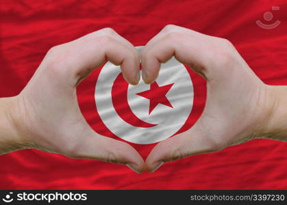 Gesture made by hands showing symbol of heart and love over tunisia flag