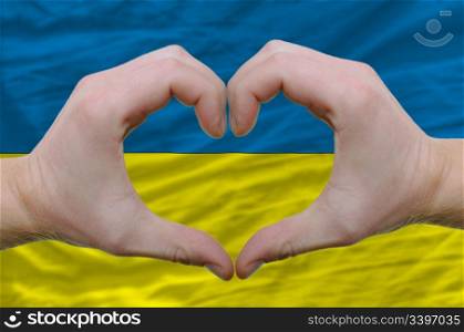 Gesture made by hands showing symbol of heart and love over ukraine flag