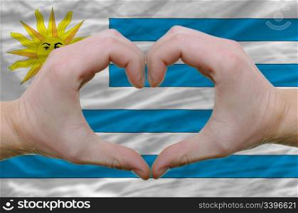 Gesture made by hands showing symbol of heart and love over uruguay flag