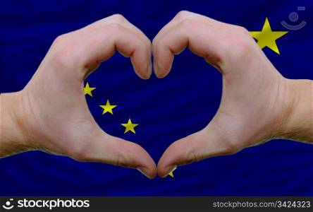 Gesture made by hands showing symbol of heart and love over us state flag of alaska