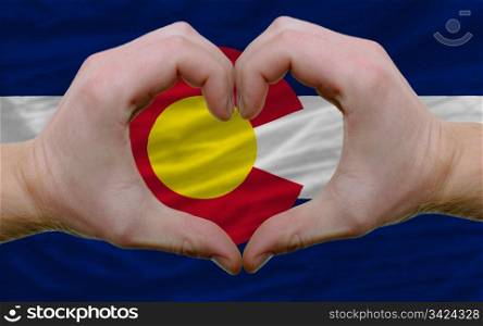 Gesture made by hands showing symbol of heart and love over us state flag of colorado