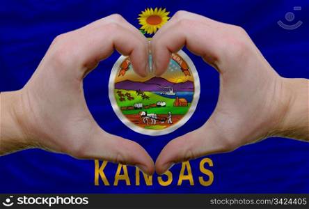 Gesture made by hands showing symbol of heart and love over us state flag of kansas