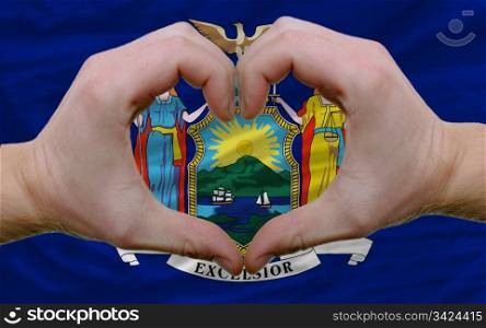 Gesture made by hands showing symbol of heart and love over us state flag of new york