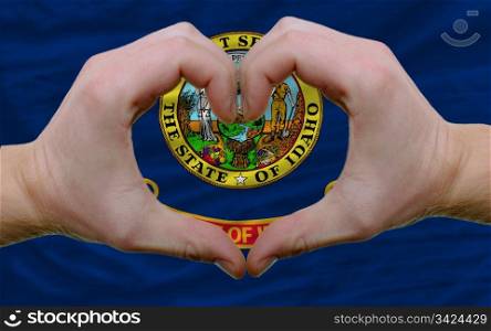 Gesture made by hands showing symbol of heart and love over us state flag of idaho