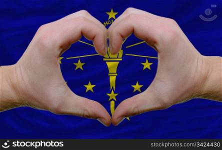 Gesture made by hands showing symbol of heart and love over us state flag of indiana