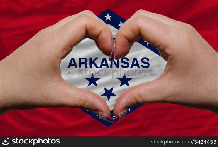Gesture made by hands showing symbol of heart and love over us state flag of arkansas