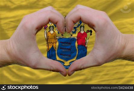 Gesture made by hands showing symbol of heart and love over us state flag of new jersey