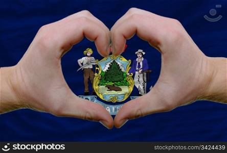 Gesture made by hands showing symbol of heart and love over us state flag of maine