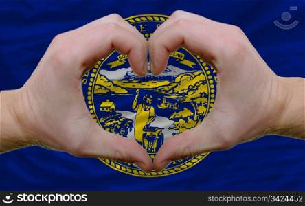 Gesture made by hands showing symbol of heart and love over us state flag of nebraska