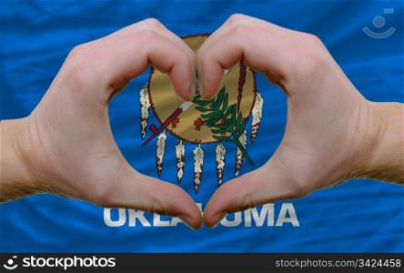 Gesture made by hands showing symbol of heart and love over us state flag of oklahoma