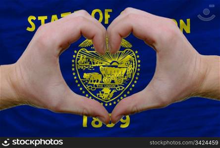Gesture made by hands showing symbol of heart and love over us state flag of oregon
