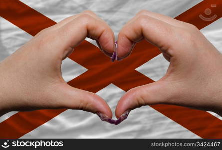 Gesture made by hands showing symbol of heart and love over us state flag of alabama