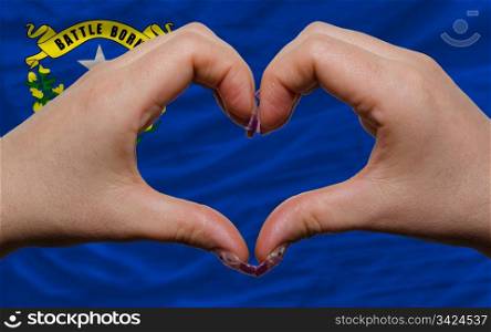 Gesture made by hands showing symbol of heart and love over us state flag of nevada
