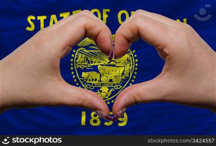 Gesture made by hands showing symbol of heart and love over us state flag of oregon