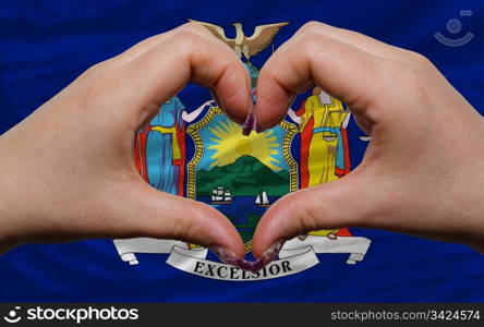 Gesture made by hands showing symbol of heart and love over us state flag of new york