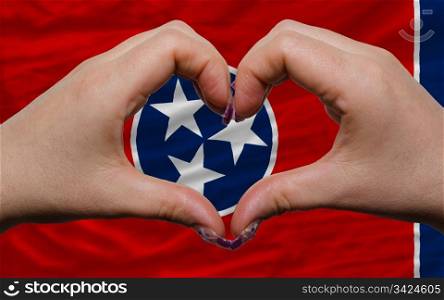 Gesture made by hands showing symbol of heart and love over us state flag of tennessee