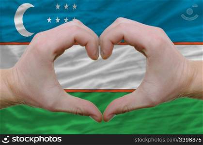 Gesture made by hands showing symbol of heart and love over uzbekistan flag