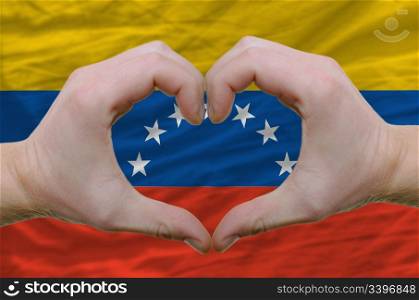 Gesture made by hands showing symbol of heart and love over venezuela flag